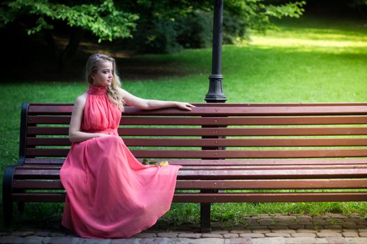 pretty girl in pink dress sits on a park bench with yellow rose