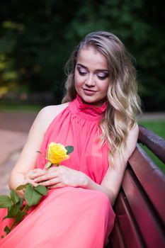 pretty girl in pink dress sits on a park bench with yellow rose