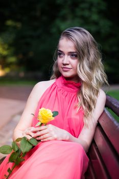 pretty girl in pink dress sits on a park bench with yellow rose