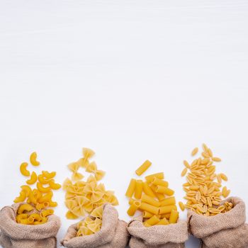 Italian foods concept and menu design . Various kind of Pasta Elbow Macaroni ,Farfalle ,Rigatoni ,gnocco Sardo in hemp sack bags setup on white wooden background with copy space.