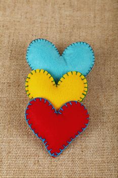 Felt craft and art, three handmade stitched toy hearts, yellow, red and blue on canvas background, close up, elevated high angle view