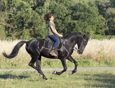 young riding girl and her black stallion in the nature