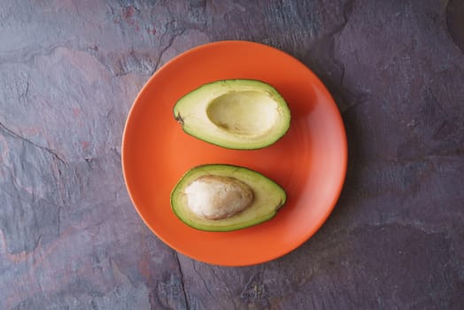 Avocado halves lie on an orange plate on a slate horizontal