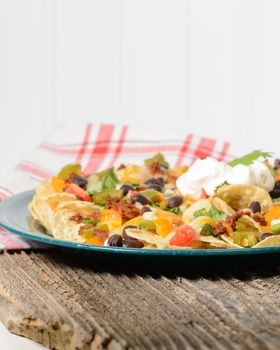 Plate of colorful nachos on a rustic wood table.