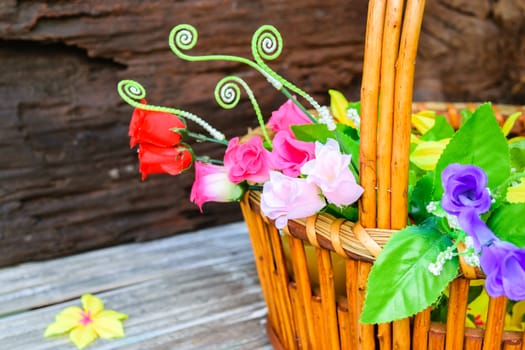 beautiful flowers plastic in a basket on brown wooden background