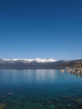 Scenic view of beautiful Lake Tahoe in Spring, landscape of the United States of America, clear water, nice sky, stone island, tree, fresh air and snow mountains