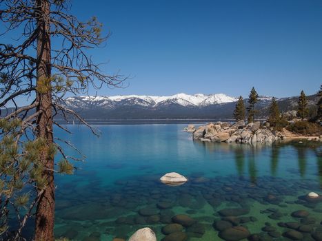 Scenic view of beautiful Lake Tahoe in Spring, landscape of the United States of America, clear water, nice sky, stone island, tree, fresh air and snow mountains