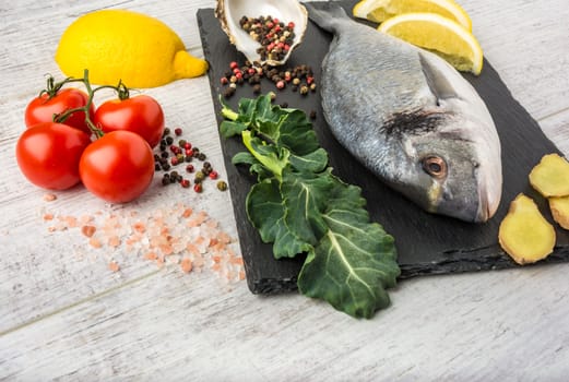 Useful dorado fish, rich in protein, vitamins, Omega 3 with vegetables, lemon and ginger, prepared for cooking on a white wooden table. 