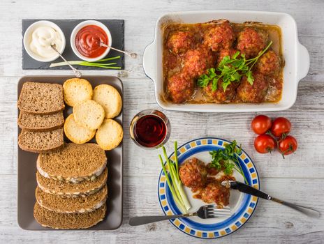 Delicious meal rich in protein and vitamins. Meatballs with tomato sauce, tomatoes, bread, mayonnaise, ketchup and a glass of wine on a white wooden background. Top view