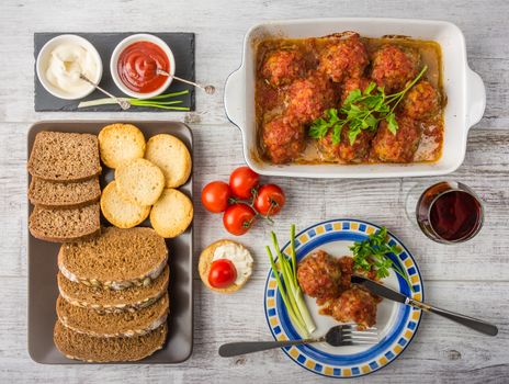 Delicious meal rich in protein and vitamins. Meatballs with tomato sauce, tomatoes, bread, mayonnaise, ketchup and a glass of wine on a white wooden background. Top view