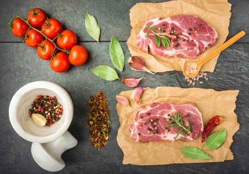 raw beef steak with spices, tomatoes on a dark table prepared for cooking top view