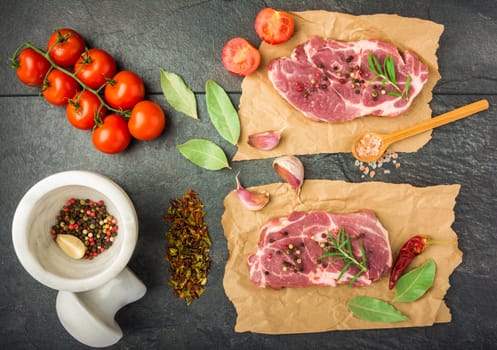 raw beef steak with spices, tomatoes on a dark table prepared for cooking top view