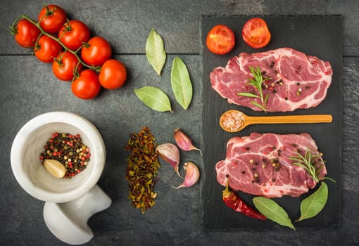 raw beef steak with spices, tomatoes on a dark table prepared for cooking top view