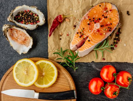 Delicious salmon steak , rich in omega 3 oil, with aromatic herbs and spices with a lemon, tomato, garlic on black background. Healthy and diet food. Top view.