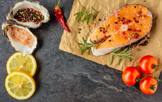 Delicious salmon steak , rich in omega 3 oil, with aromatic herbs and spices with a lemon, tomato, garlic on black background. Healthy and diet food. Top view.