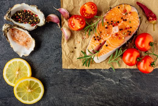 Delicious salmon steak , rich in omega 3 oil, with aromatic herbs and spices with a lemon, tomato, garlic on black background. Healthy and diet food. Top view.