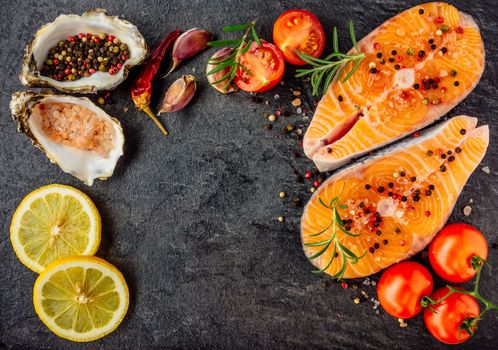 Delicious salmon steak , rich in omega 3 oil, with aromatic herbs and spices with a lemon, tomato, garlic on black background. Healthy and diet food. Top view.