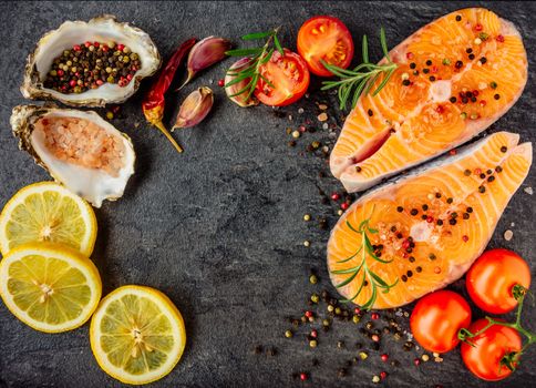 Delicious salmon steak , rich in omega 3 oil, with aromatic herbs and spices with a lemon, tomato, garlic on black background. Healthy and diet food. Top view.