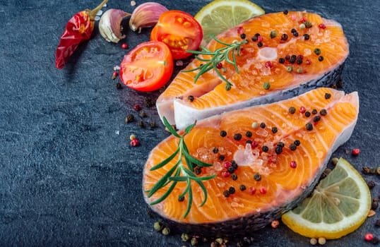 Delicious salmon steak , rich in omega 3 oil, with aromatic herbs and spices with a lemon, tomato, garlic on black background. Healthy and diet food.