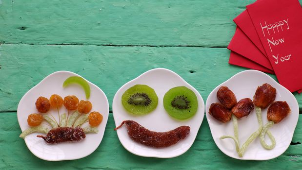 Vietnamese food for Vietnam Tet holiday, also lunar new year of Asia, colorful preserved fruit as kiwi, damson jam, or coconut jam set up on white plate with green wood background make art