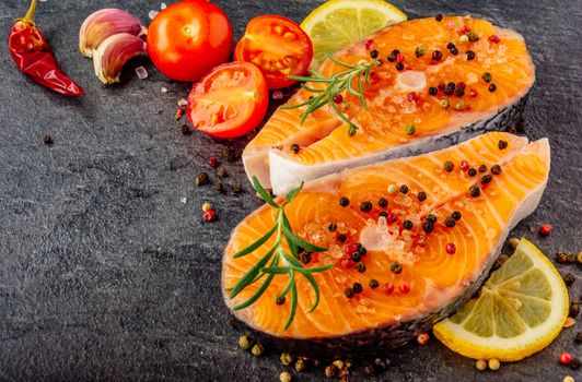 Delicious salmon steak , rich in omega 3 oil, with aromatic herbs and spices with a lemon, tomato, garlic on black background. Healthy and diet food. Close-up