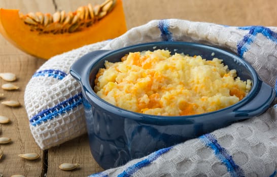 millet porridge with pumpkin in blue bowl in a kitchen towel, pumpkin and pumpkin seeds on a  wooden table closeup