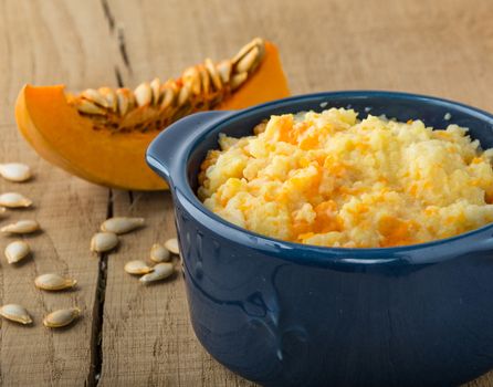 millet porridge with pumpkin in blue bowl, pumpkin and pumpkin seeds on a  wooden table closeup