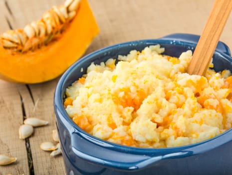 millet porridge with pumpkin in blue bowl, pumpkin and pumpkin seeds on a  wooden table closeup