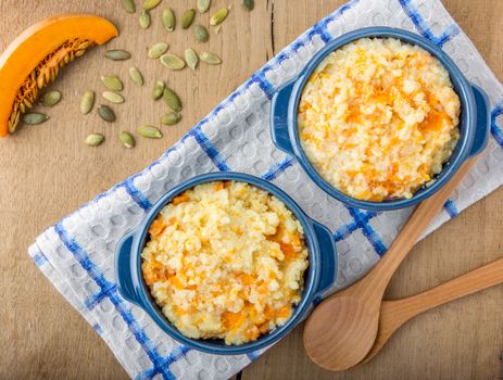 millet porridge with pumpkin in blue bowl on a kitchen towel, pumpkin seeds and wooden spoons  on a wooden table top view