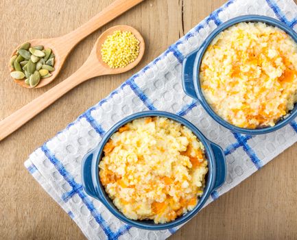 millet porridge with pumpkin in blue bowl on a kitchen towel, pumpkin seeds and millet in a wooden spoon  on a wooden table top view