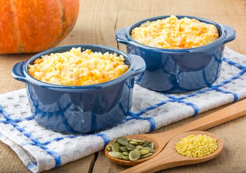 millet porridge with pumpkin in blue bowl on a kitchen towel, pumpkin seeds and millet in a wooden spoon and pumpkin on a wooden table