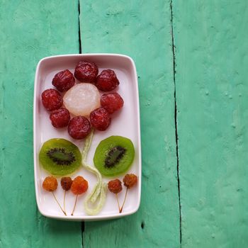 Vietnamese food for Vietnam Tet holiday, also lunar new year of Asia, colorful preserved fruit as kiwi, damson jam, or coconut jam set up on white plate with green wood background make art