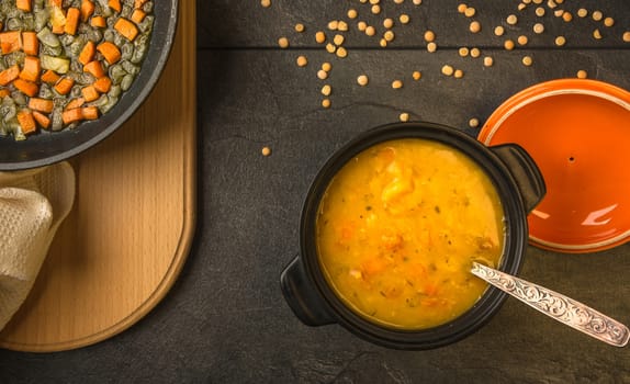 pea soup with carrots and onions in a black pot on a dark table top view