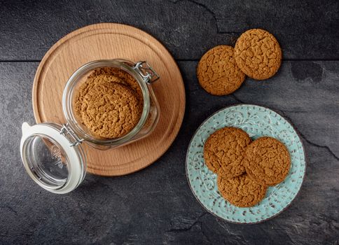 Oat cookies lay on a plate and bank with oatmeal cookies standing on a wooden board top view