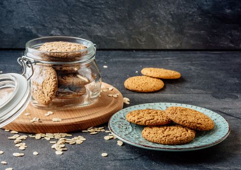 Oat cookies lay on a plate and bank with oatmeal cookies standing on a wooden board.