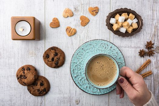 Women drinking coffee with milk. Cookies, sugar, cinnamon, star anise and candle lying on a white wooden table top view