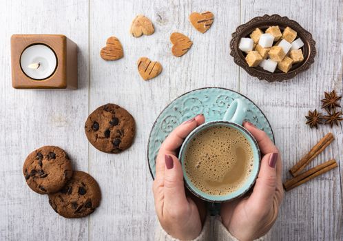 Women drinking coffee with milk. Cookies, sugar, cinnamon, star anise and candle lying on a white wooden table top view