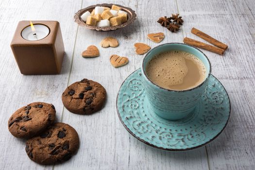 Coffee with milk, cookies, sugar, cinnamon, star anise and candle lying on a white wooden table