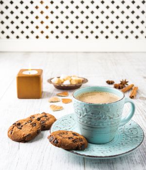 Coffee with milk, cookies, sugar, cinnamon, star anise and candle lying on a white wooden table