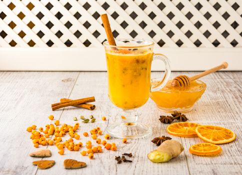 sea buckthorn tea with honey, sea buckthorn , cinnamon, carnation and orange slices on a white wooden table