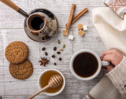 woman drinking coffee with cookies, sugar and honey. coffee maker, cinnamon,star anise and cardamon lying on a white wooden table. 