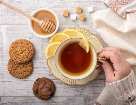 woman drinking tea with lemon . cookies, sugar , honey lying on a white wooden table. 