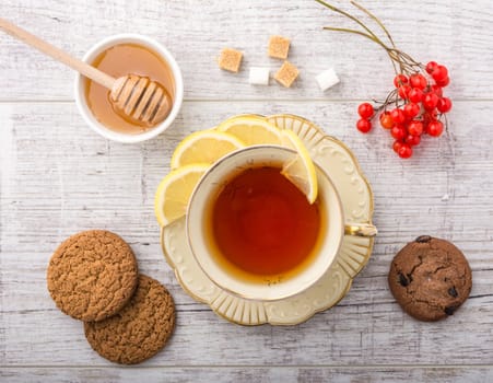 tea with lemon . cookies, sugar , honey and viburnum lying on a white wooden table. 