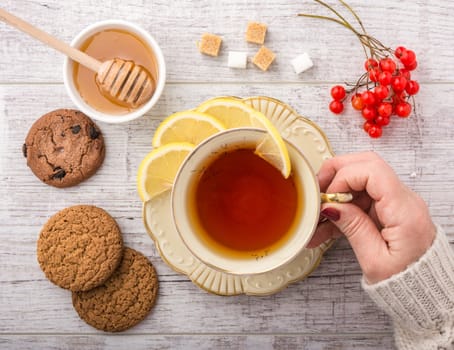 woman drinking tea with lemon . cookies, sugar , honey and viburnum lying on a white wooden table. 