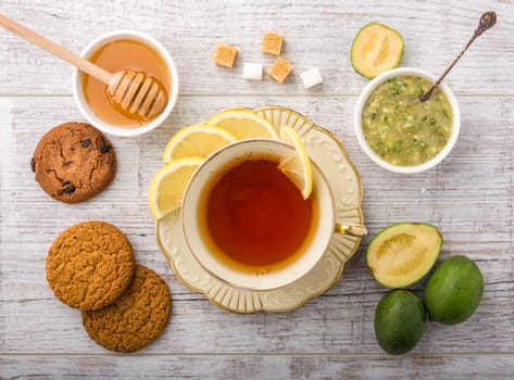  tea with lemon . cookies, sugar , honey, feijoa and jam feijoa  lying on a white wooden table. 