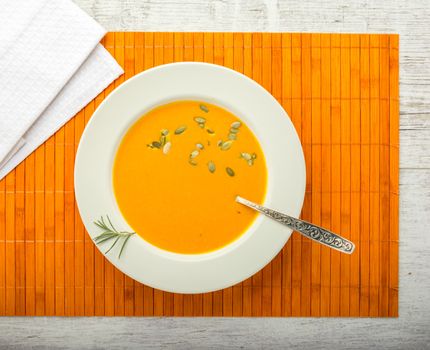 pumpkin cream soup with pumpkin seeds in a white plate with a spoon on a orange napkin closeup