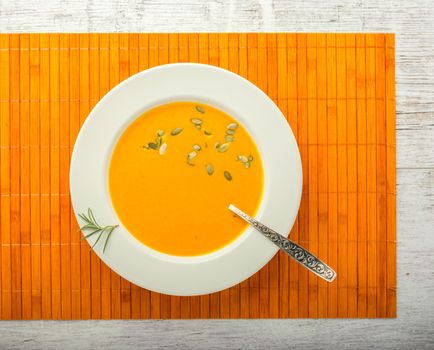 pumpkin cream soup with pumpkin seeds in a white plate with a spoon on a orange napkin closeup