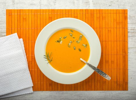 pumpkin cream soup with pumpkin seeds in a white plate with a spoon on a orange napkin closeup