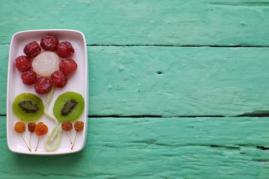 Vietnamese food for Vietnam Tet holiday, also lunar new year of Asia, colorful preserved fruit as kiwi, damson jam, or coconut jam set up on white plate with green wood background make art