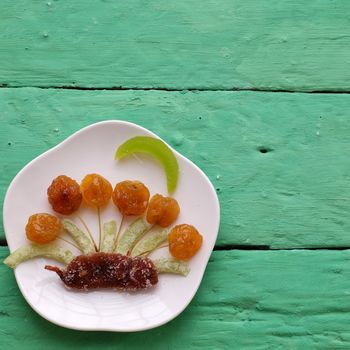 Vietnamese food for Vietnam Tet holiday, also lunar new year of Asia, colorful preserved fruit as kiwi, damson jam, or coconut jam set up on white plate with green wood background make art